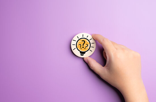 Hand holding wooden label with light bulb and question mark sign icon on purple background. Innovative solution for business concept. Creative thinking ideas for learning, planning, and working.