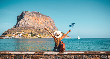 Happy woman tourist with bag and flag enjoying vacation in Greece- Monemvasia island - obrazy, fototapety, plakaty