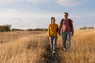 Young couple hiking through autumn fields and hills during warm day. Weekend, leisure, sport