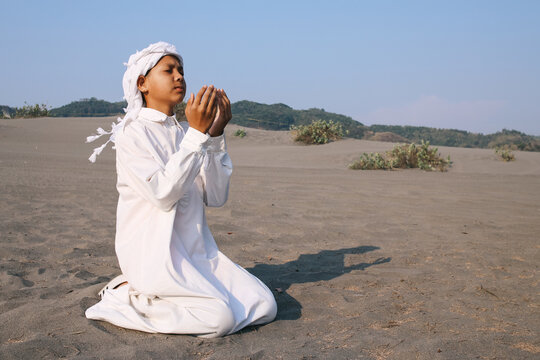 Muslim Asian young boy praying on knees at the sand dunes 