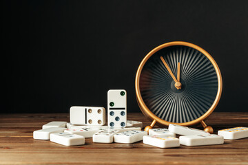 Domino tiles and clock on wooden table against black background