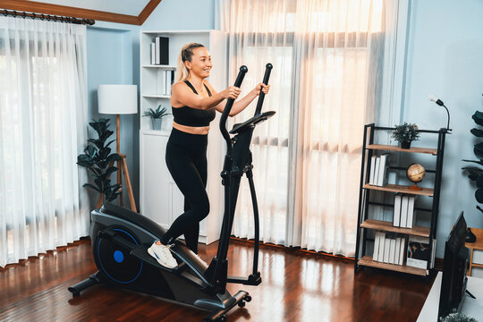 Active senior woman running on elliptical running machine at home portrait in full body shot as fitness healthy lifestyle and body care after retirement for pensioner. Clout