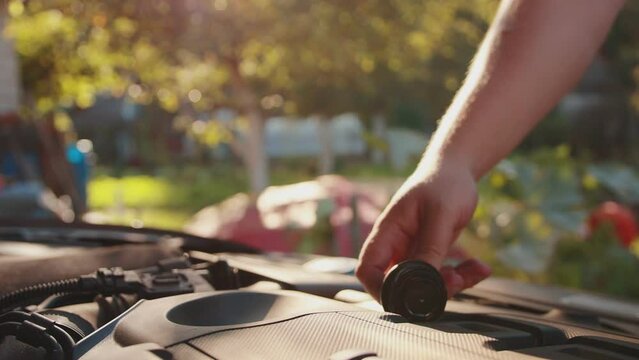 A man places the oil filler cap on the engine. The concept of replacing old oil with new one against the backdrop of the sun, slow motion. Copy space for text, industry