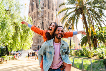 Multiracial beautiful happy couple of lovers dating at Sagrada Familia, Barcelona - Multiethnic tourists travelling in Europe and visiting a city in Spain, concepts about tourism and people lifestyle - obrazy, fototapety, plakaty