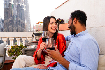 Multiracial beautiful happy couple of lovers dating on rooftop balcony at Sagrada Familia, Barcelona - Multiethnic people having romantic aperitif on a terrace with city view , concept about tourism - obrazy, fototapety, plakaty