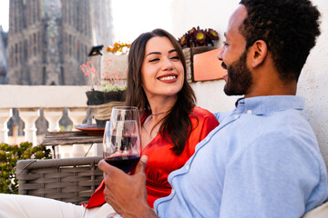 Multiracial beautiful happy couple of lovers dating on rooftop balcony at Sagrada Familia, Barcelona - Multiethnic people having romantic aperitif on a terrace with city view , concept about tourism - obrazy, fototapety, plakaty