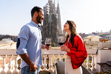 Multiracial beautiful happy couple of lovers dating on rooftop balcony at Sagrada Familia, Barcelona - Multiethnic people having romantic aperitif on a terrace with city view , concept about tourism
