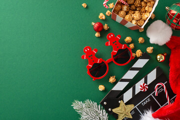 Festive movie debut for New Year, filled with kid-friendly elements. Top view of clapper, gingerbread man-inspired party glasses, popcorn, frosty fir twig and more on green backdrop with space for ad