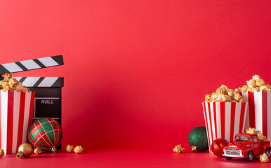 Enjoy cozy Christmas movie night at home with delivered popcorn. Side view image of table with striped popcorn boxes, ornaments, clapper, mini retro car against a red wall. Ad space available - obrazy, fototapety, plakaty