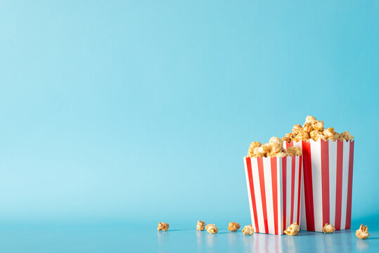 Plan a cinematic night with friend and savory snacks. A side view image of a table graced with delectable popcorn in striped boxes against pastel blue wall, leaving space for movie ads