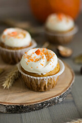 Autumn pumpkin cupcakes with orange sprinkles on top on natural wooden background with real pumpkin behind close up selective focus