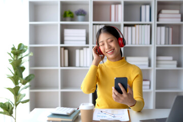 ASian woman wearing headphones and using a phone enjoying listening to music.