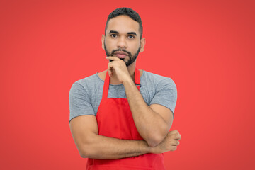 Handsome hispanic waiter with apron on red background