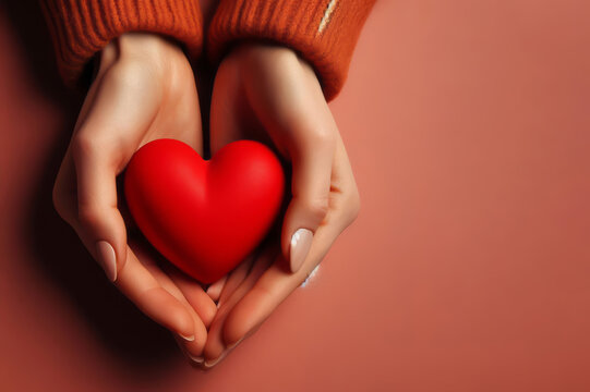 hands hold a red heart on a orange background
