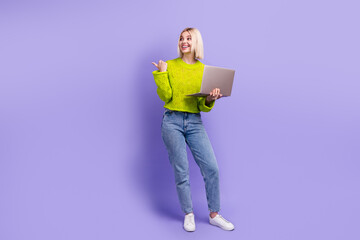 Full length photo of cheerful dreamy woman dressed knitted sweater studying device thumb empty space isolated violet color background