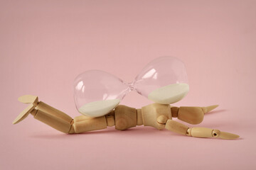 Wooden mannequin lying under hourglass on pink background - Concept of stopping time, health and...