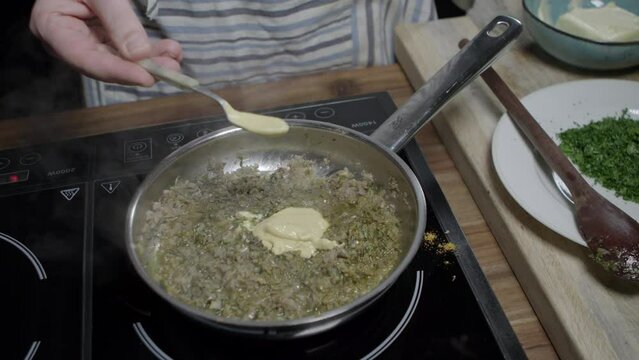 A chef puts yellow mustard into a metal pan. Preparing delicious caf&eacute; de paris sauce for steaks.
