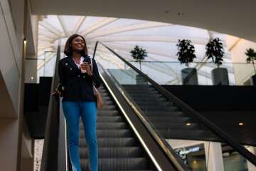 In a joyful mood, the formally dressed black business woman holds her coffee and phone while...