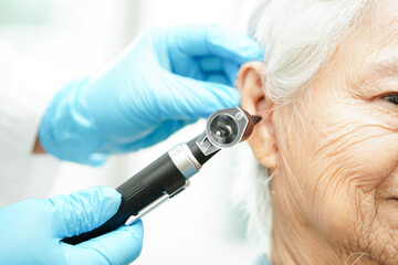 Otolaryngologist or ENT physician doctor examining senior patient ear with otoscope, hearing loss problem. - obrazy, fototapety, plakaty