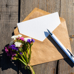 Static flowers and an envelope with an empty postcard. An empty postcard made of white paper and an envelope made of kraft paper, a letter with a place to copy the text, a greeting or an invitation.