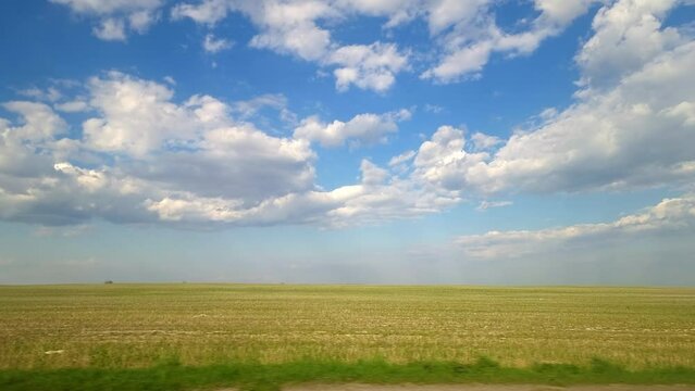 Vehicle point-of-view The view through the side window while traveling by car. The view of the passenger in the car through the window. Fields and blue sky with clouds. Beautiful nature of the flat