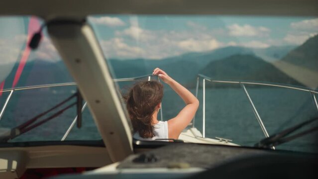 Modern yacht with lady on deck sails to large mountains on summer day. Woman with waving hair rides motorboat on weekend. Happy time at seaside
