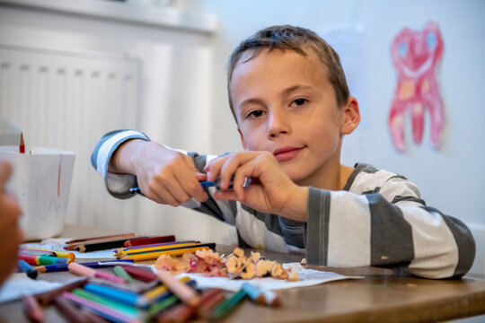 child preparing for schoolwork. the boy sewing crayons. he is sitting bihind floor sitting desk.