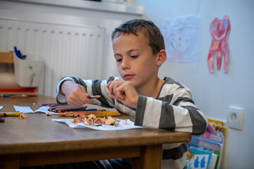 child preparing for schoolwork. the boy sewing crayons. he is sitting bihind floor sitting desk.