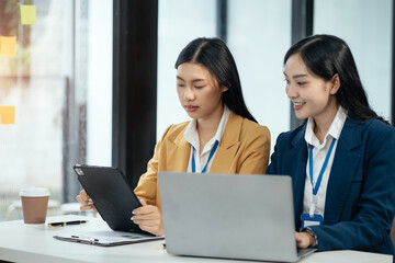 Business documents on office table with tablet and laptop computer and chart and two colleagues discussing data in office.