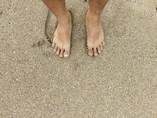 man's striped feet on the white sand of the beach while the sky is clear