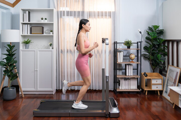 Fototapeta na wymiar Full length side view of energetic and strong athletic asian woman running running machine at home. Pursuit of fit physique and commitment to healthy lifestyle with home workout and training. Vigorous