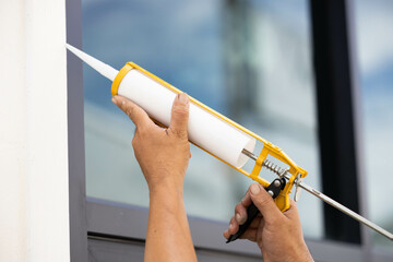 Builders are using a silicone caulking gun to fill a leak between glass and aluminum.