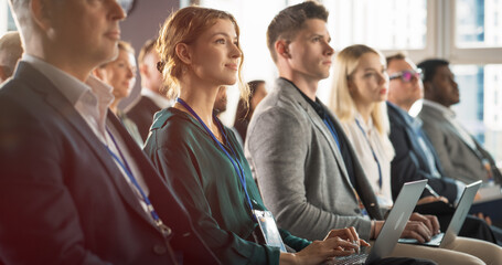 Young Woman Sitting in Crowded Audience at Business Conference. Female Delegate Smiling and Using...