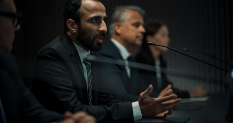 Multiethnic Male Head Of Political Delegation Speaking At International Economic Forum Press Conference. High-Profile Politician Reporting On Successful Agreements. Focused Diverse Delegates Listening