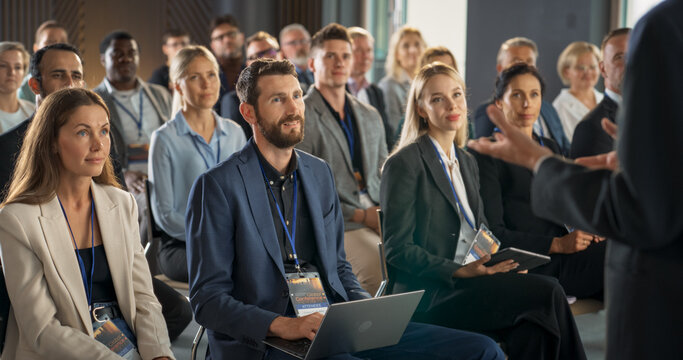 Back View Of Biopharma CEO Gesturing And Presenting To Audience Of Diverse Industry Leaders. Male And Female Attendees Listening To Presentation About Biotechnology On International Medical Summit.