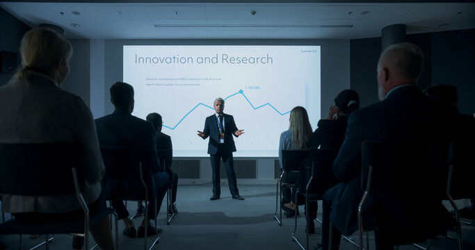Corporate Event: Caucasian Male Tech CEO Giving Presentation To Colleagues or Investors In the Conference Room Of Innovative Startup Office. Man Talking About Business Objectives and Profit Margins.