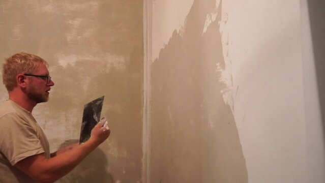 Male builder use metal spatula for putty walls, repairman filling spatula with spackling paste and covering cement wall surface. Builder leveling wall and angle Renovation work in Residential Premises