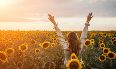 Woman in Sunflower Field: Happy girl in a straw hat posing in a vast field of sunflowers at sunset, enjoy taking picture outdoors for memories. Summer time. - obrazy, fototapety, plakaty