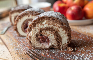 Swiss roll with buttercream and cherries on wooden table