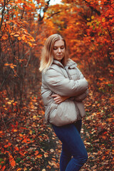 Woman walking in autumn forest among yellow and red leaves. Warm October weather, walk in the fresh air.