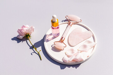 Rose Oil Cosmetic Bottle, Gua Sha Scraper, Quartz Roller Massager on Ceramic Tray with Rose Petals. home care, massage.