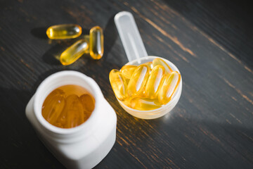 Omega 3 fish oil yellow capsules in a plastic measuring spoon, dietary supplement on dark wooden board, healthy eating concept, close up view