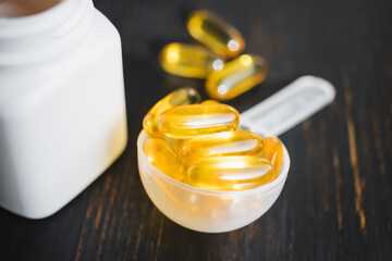 Omega 3 fish oil yellow capsules in a plastic measuring spoon, dietary supplement on dark wooden board, healthy eating concept, close up view