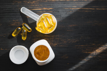 Omega 3 fish oil yellow capsules in a plastic measuring spoon, dietary supplement on dark wooden board, healthy eating concept, top view