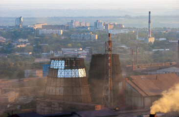 Two cooling towers of metallurgical plant with the city on background