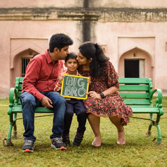 Indian couple posing for maternity baby shoot with their 5 year old kid. The couple is posing in a lawn with green grass and the woman is flaunting her baby bump in Lodhi Garden in New Delhi, India - obrazy, fototapety, plakaty
