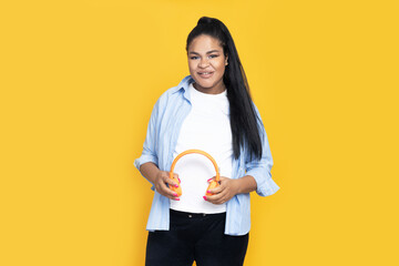 Pregnant African American woman with headphones on yellow background.