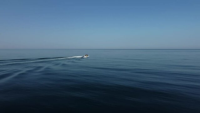Aerial woman on wakeboard. Young athlete riding wakesurf behind boat towing wave. Drone shot of a girl wakeboarding in the calm sea. Woman learning to wake board on deep blue and crystal clear sea.