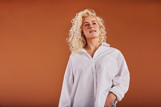 Smiling blonde woman standing in a white shirt on an orange background