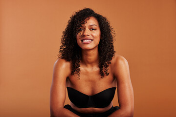Young black woman wearing a strapless bra smiling on an orange background
